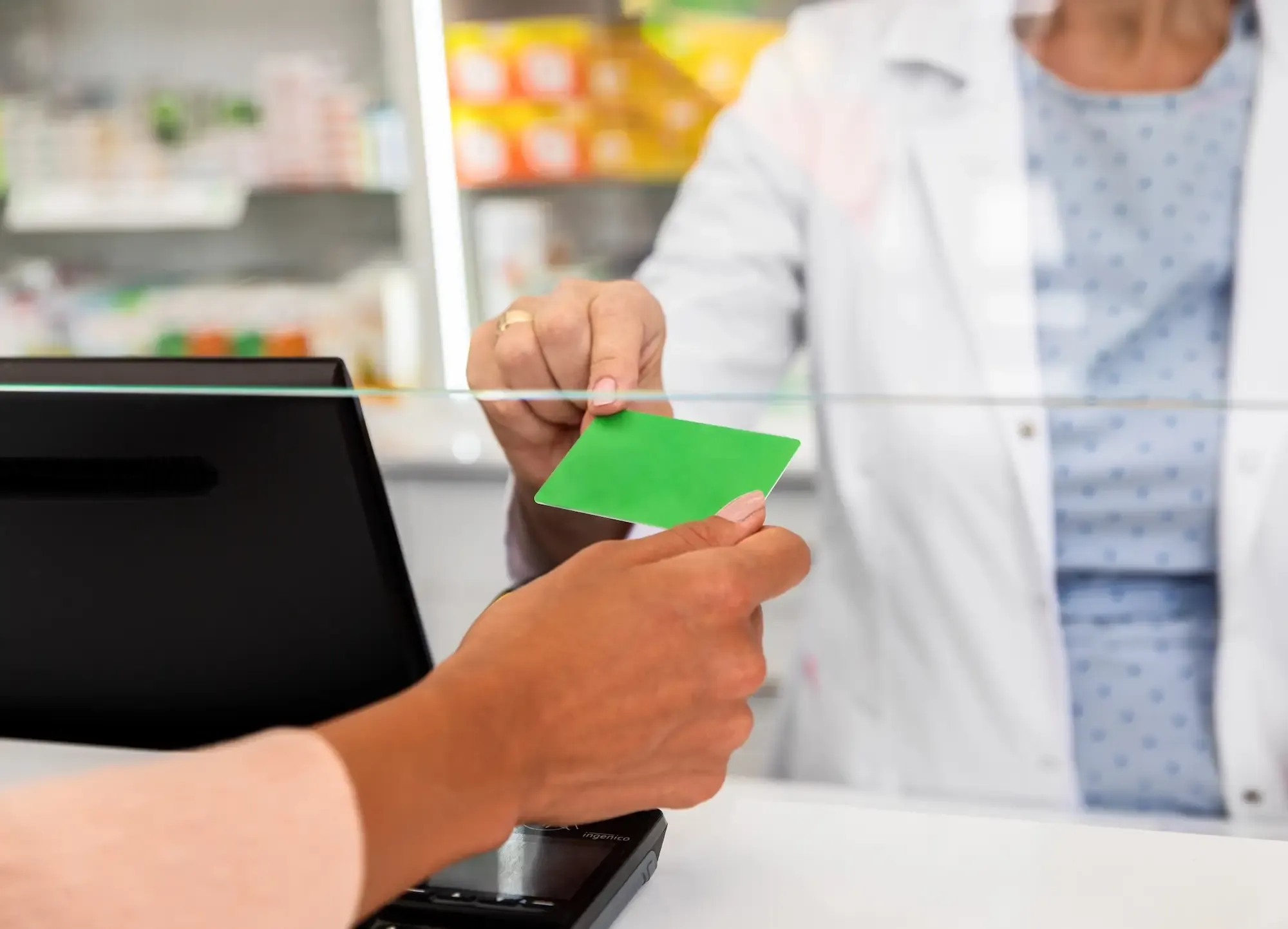 A person handing their green Carte Vitale card to a pharmacist at a French pharmacy counter